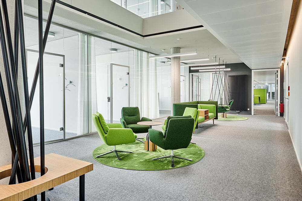 Moderne Büro-Lounge mit grünen Sesseln und Sofas von Brunner, Teppichen in Grasoptik und Glastrennwänden in einem Open-Space-Büro.