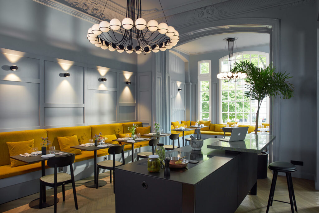 Elegantes Restaurant im Stilwerk Hotel Heimhude mit leuchtend gelben Sitzbänken, schwarzen Stühlen von Gubi und modernen Leuchten von Flos. (c) stilwerk Foto: T. Baermann