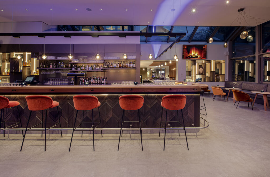 Stilvolle Bar der Blauen Eule in Iserlohn mit dunkler Holzverkleidung, roten Samtbarhockern von Freifrau und moderner Beleuchtung.
