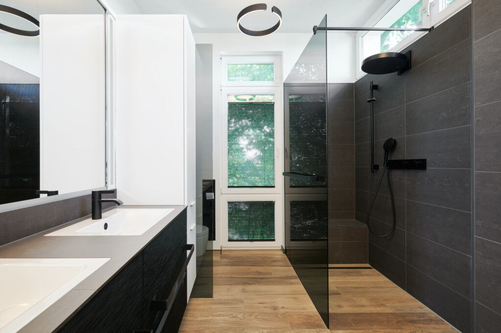 Modernisiertes Badezimmer in einem Haus im Sauerland mit bodengleicher Dusche, schwarzen Armaturen von Gessi und großformatigen Fliesen in Natursteinoptik.