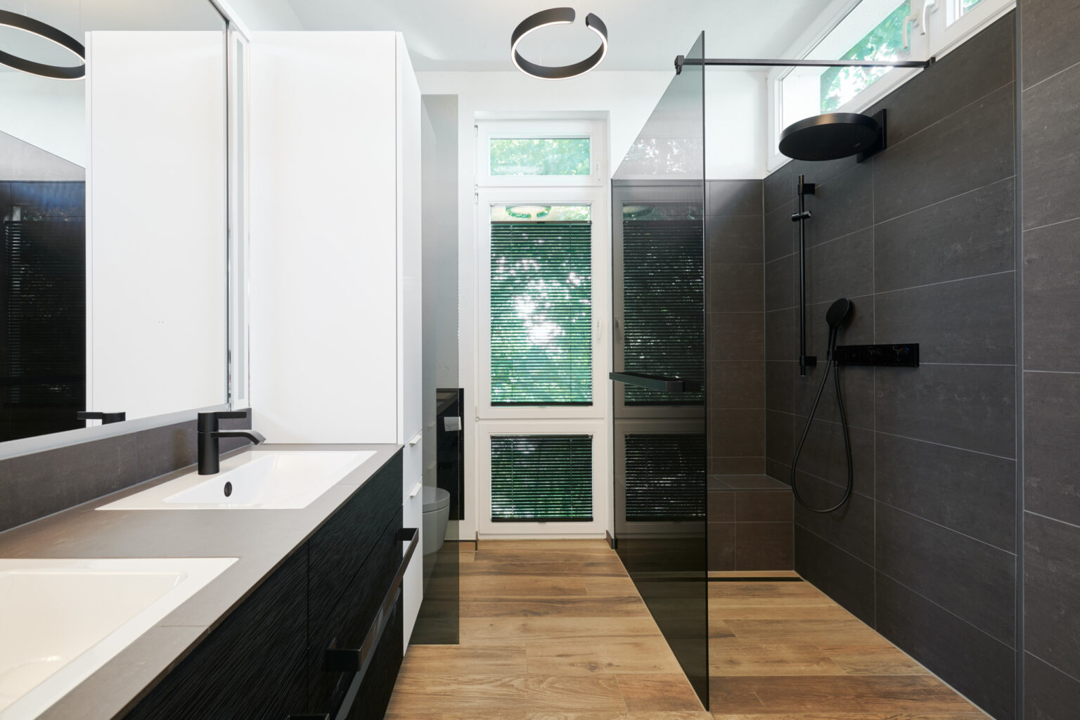Modernisiertes Badezimmer in einem Haus im Sauerland mit bodengleicher Dusche, schwarzen Armaturen von Gessi und großformatigen Fliesen in Natursteinoptik.