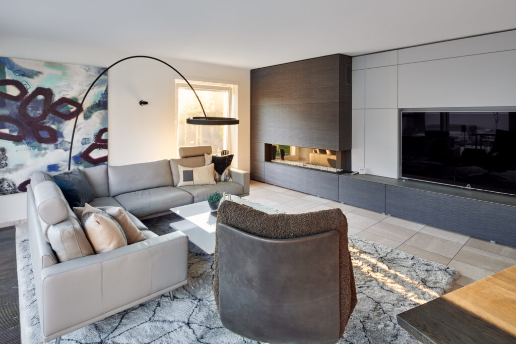 Neugestalteter Wohnbereich mit beiger Ledercouch von Walter Knoll, gemütlichem Sessel von Jori und moderner Kaminverkleidung in einem Haus im Sauerland.