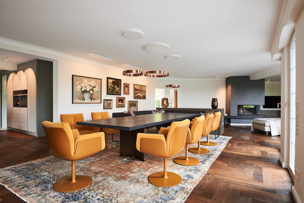 Modernisierter Essbereich in einem Haus im Sauerland, mit einem maßgefertigten Esstisch und senfgelben Drehsesseln von Walter Knoll, kombiniert mit Occhio-Leuchten.